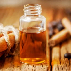 A small glass bottle filled with amber-colored liquid, surrounded by cinnamon sticks and bread.