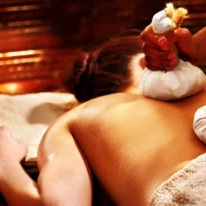 Person receiving a relaxing herbal compress massage on their back.