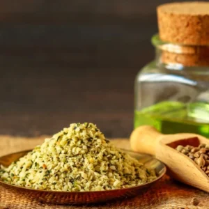 A pile of crushed herbs on a wooden plate with a jar and wooden scoop in the background.