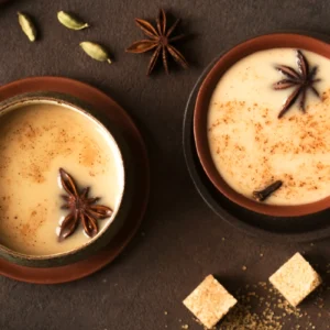 Two cups of spiced chai tea with star anise and sugar cubes.
