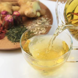 Pouring herbal tea into a glass cup with ingredients in the background.