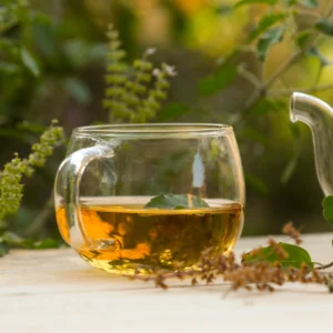 A glass cup filled with herbal tea on a white surface outdoors.