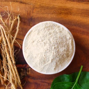 Bowl of white powder with roots and green leaf on wooden surface.