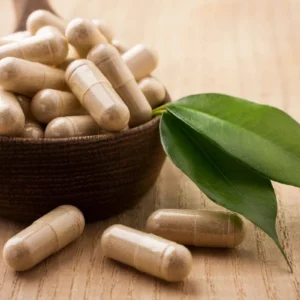 Herbal supplement capsules in a wooden bowl with green leaves.