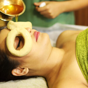 A woman receiving Ayurvedic oil therapy with a herbal ring on her forehead.
