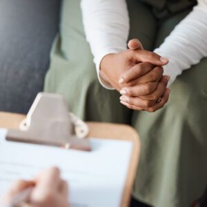 Person sitting with clasped hands during a consultation.