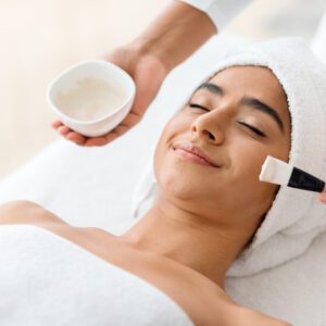 Woman enjoying a facial treatment with a brush and cream.