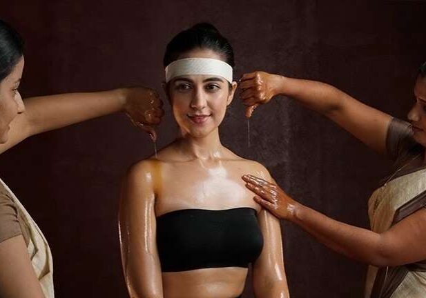 A woman with a white headband and black tube top being massaged with oil.