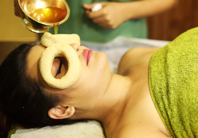 A woman receiving Ayurvedic oil therapy with a herbal ring on her forehead.