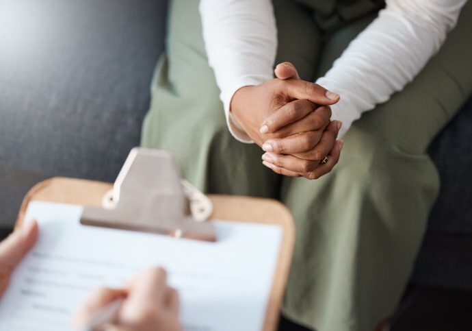 Person sitting with clasped hands during a consultation.