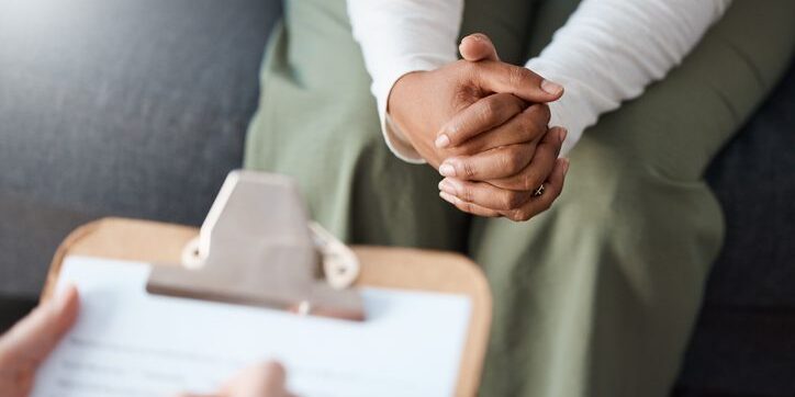 Person sitting with clasped hands during a consultation.