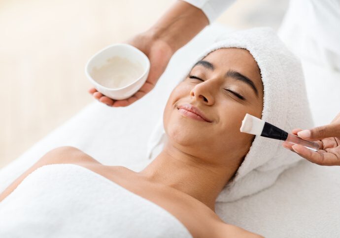 Woman enjoying a facial treatment with a brush and cream.