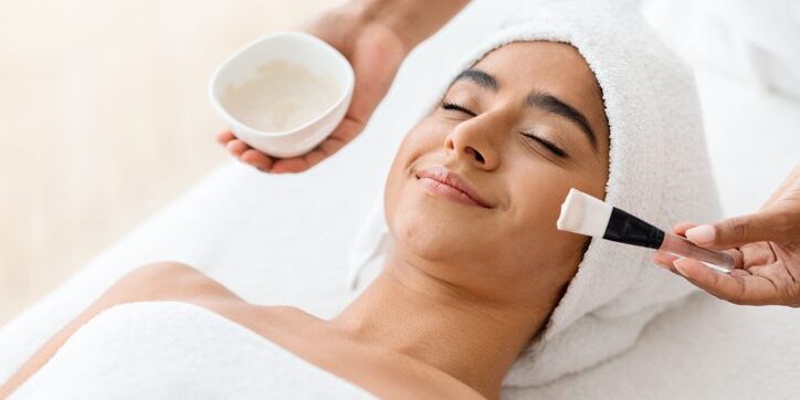 Woman enjoying a facial treatment with a brush and cream.