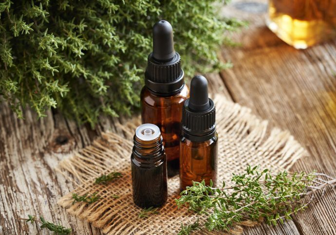 Three amber dropper bottles on a woven mat with greenery nearby.