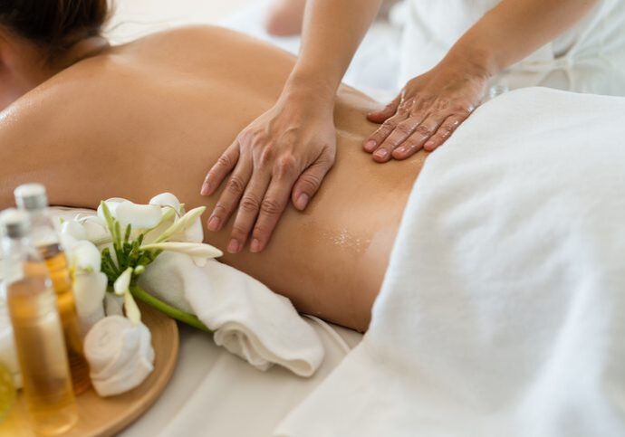 Person receiving a relaxing back massage with flowers nearby.